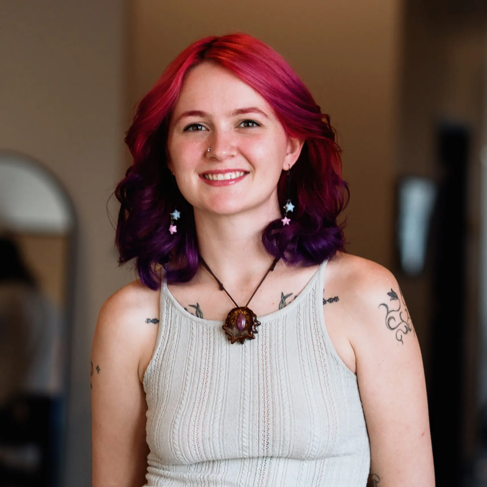 Person with vibrant hair and tattoos smiling