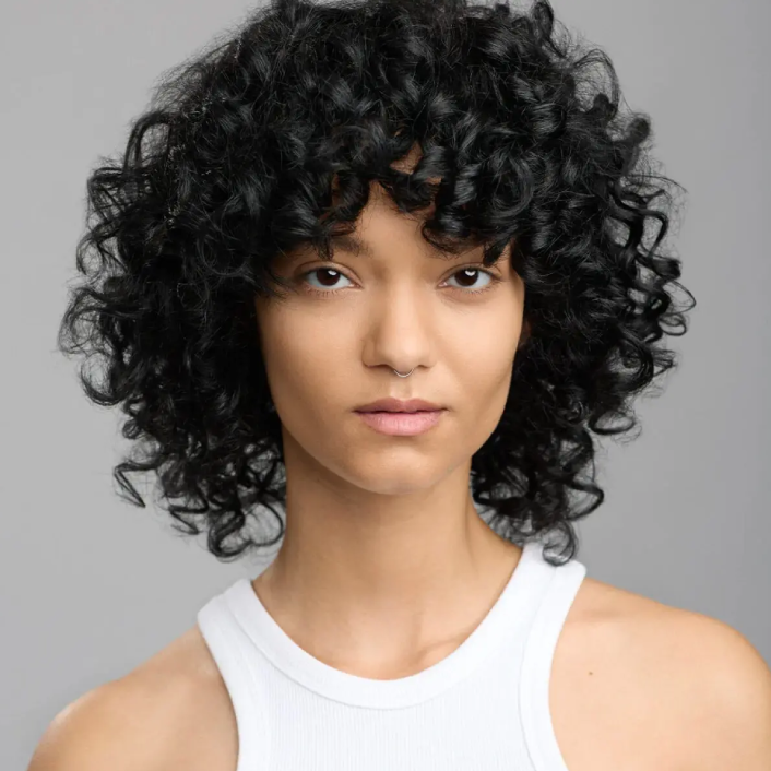 Portrait of a woman with curly hair and a white top.